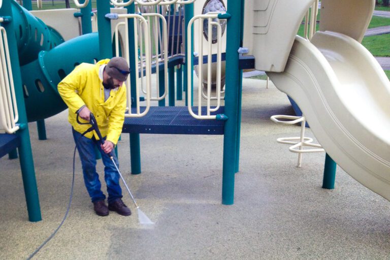 worker power washing safety surface at a playground.