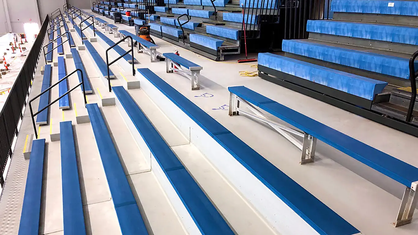 AquaSeal Deck Armor safety surfacing applied to indoor pool bleachers with blue non-slip seating surfaces and black handrails for improved traction and safety
