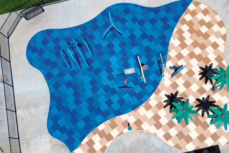Aerial view of a splash pad resurfaced by AquaSeal Resurfacing LLC, featuring blue AquaTile mosaic-style safety surfacing beside a tan geometric deck area and play features.